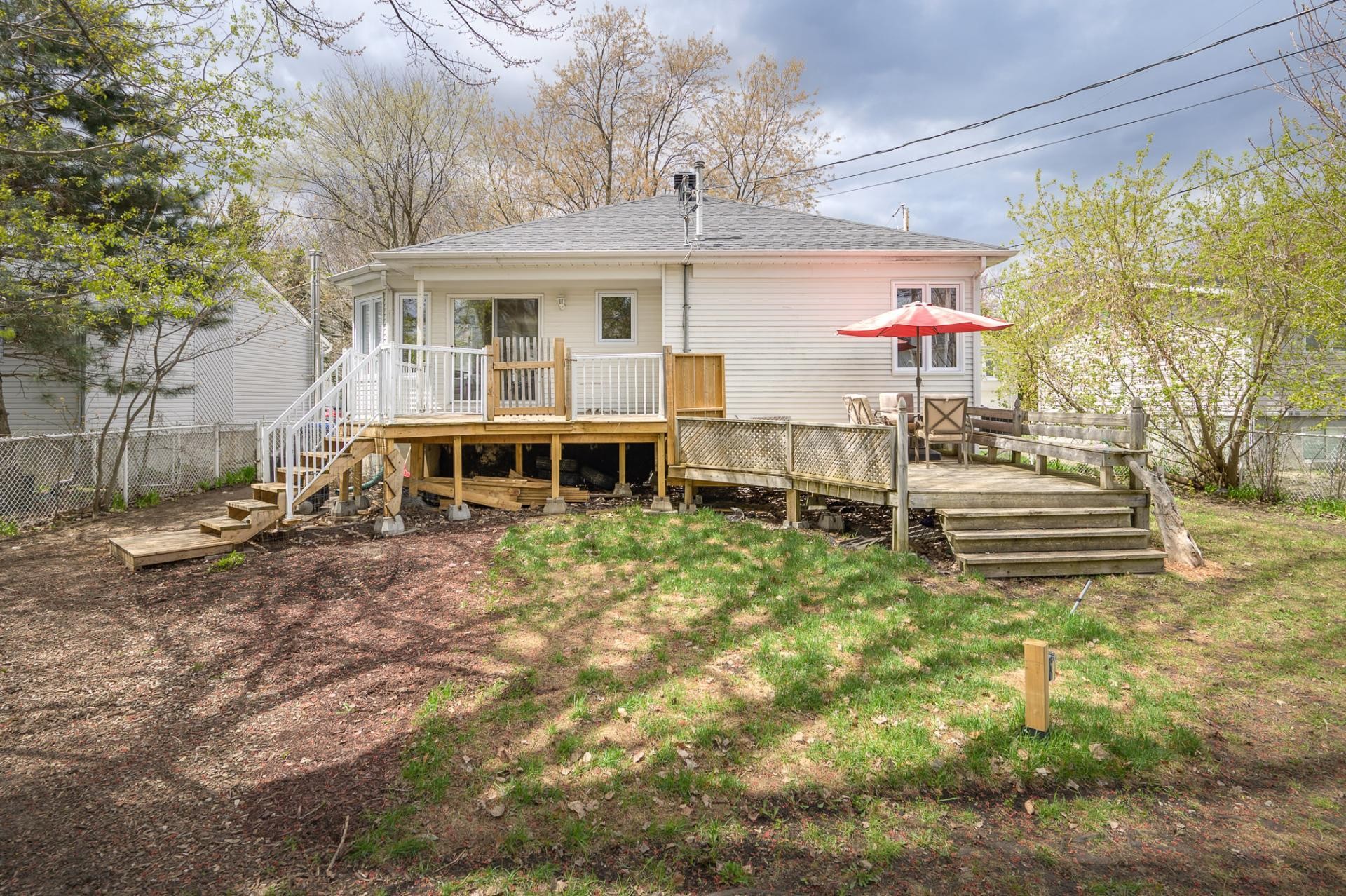Rear of house showing the wraparound deck with red patio umbrella, outdoor dining area, deck stairs to the yard
