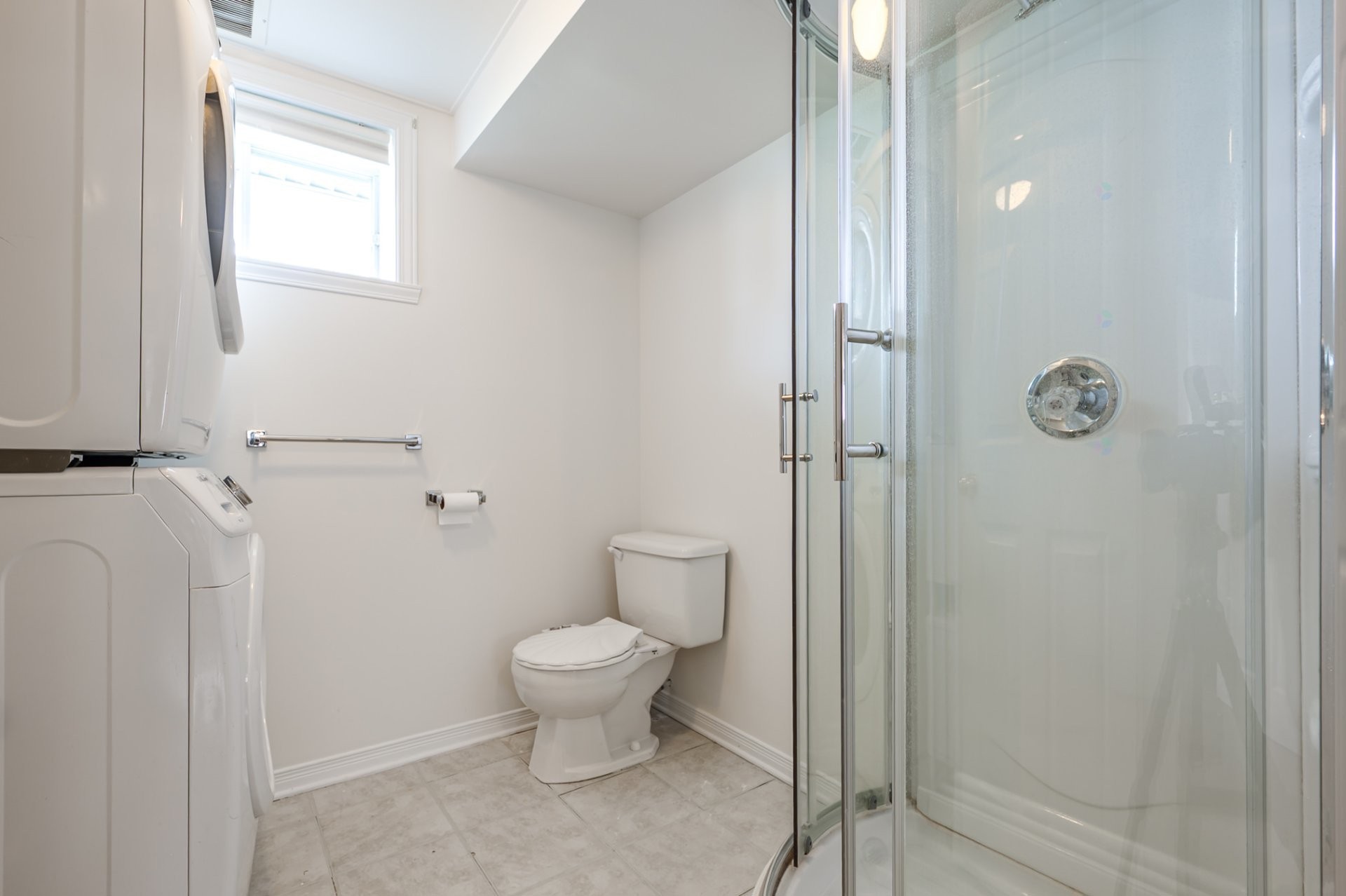 Basement bathroom with stacked washer and dryer, glass shower, toilet