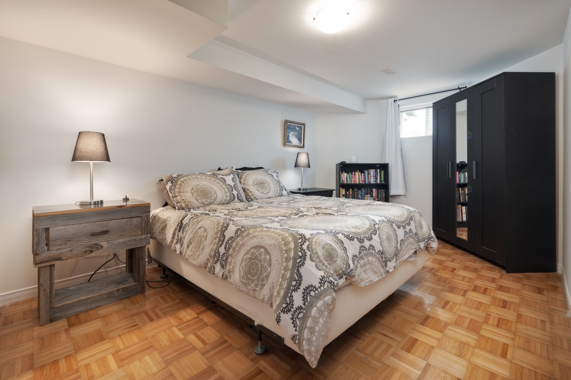 Basement bedroom with parquet floors, made bed, IKEA wardrobes, bookshelves