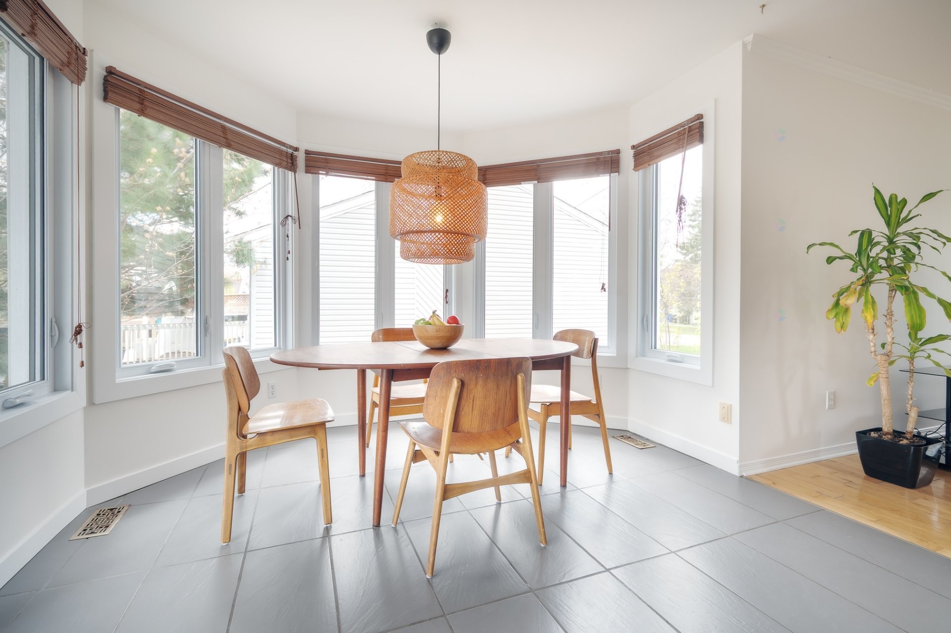South-facing dining bay with wraparound windows, wooden round table and chairs, sun streaming through
