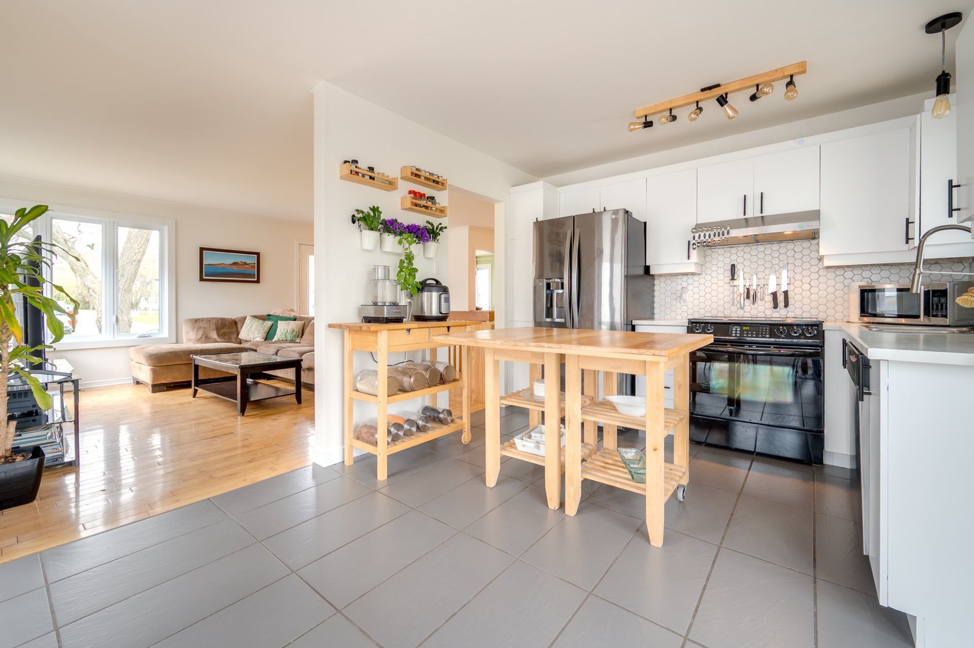 Open-plan main floor — kitchen with butcher-block island in foreground, living room with sectional visible through the opening, wood floors throughout